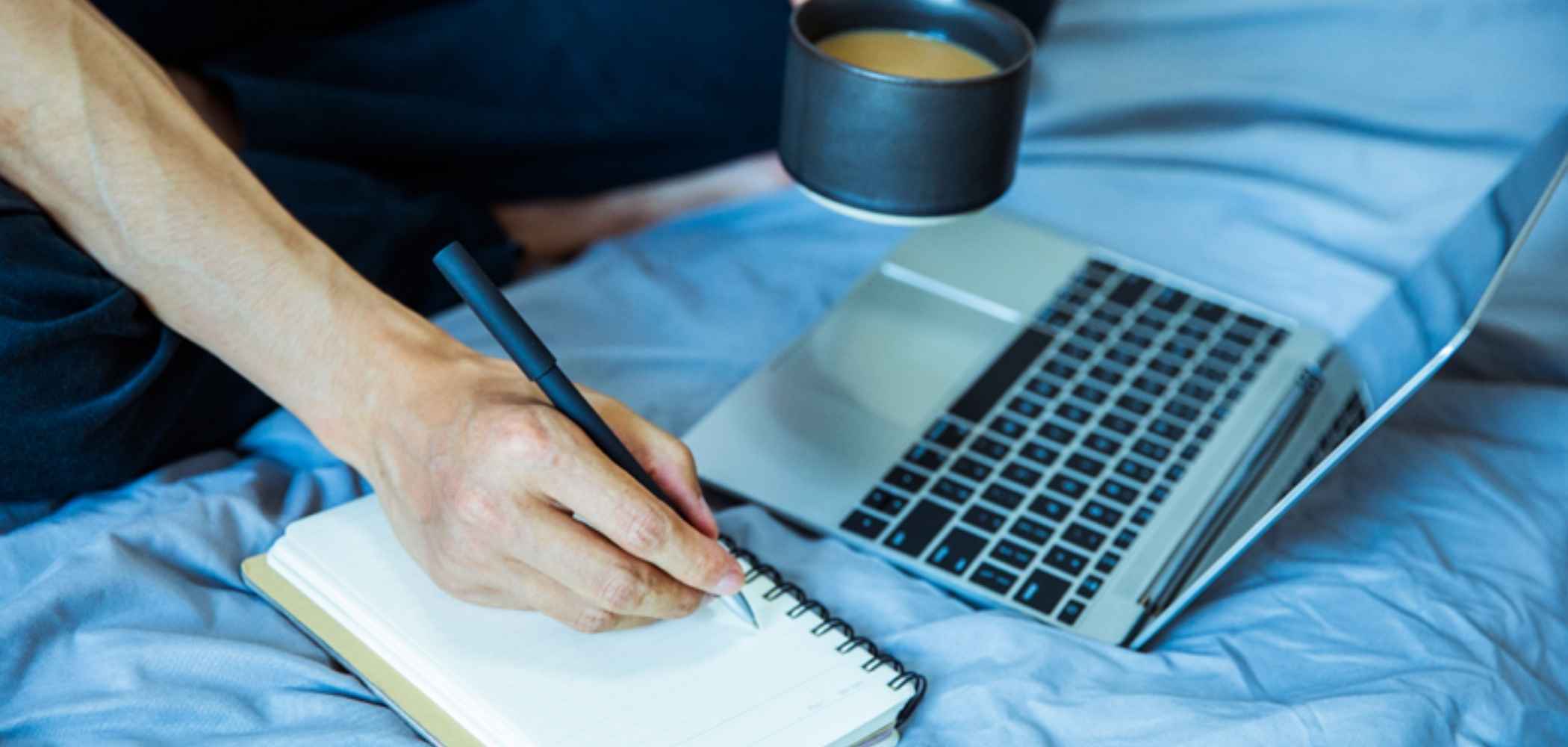 man writing on notepad while looking at computer